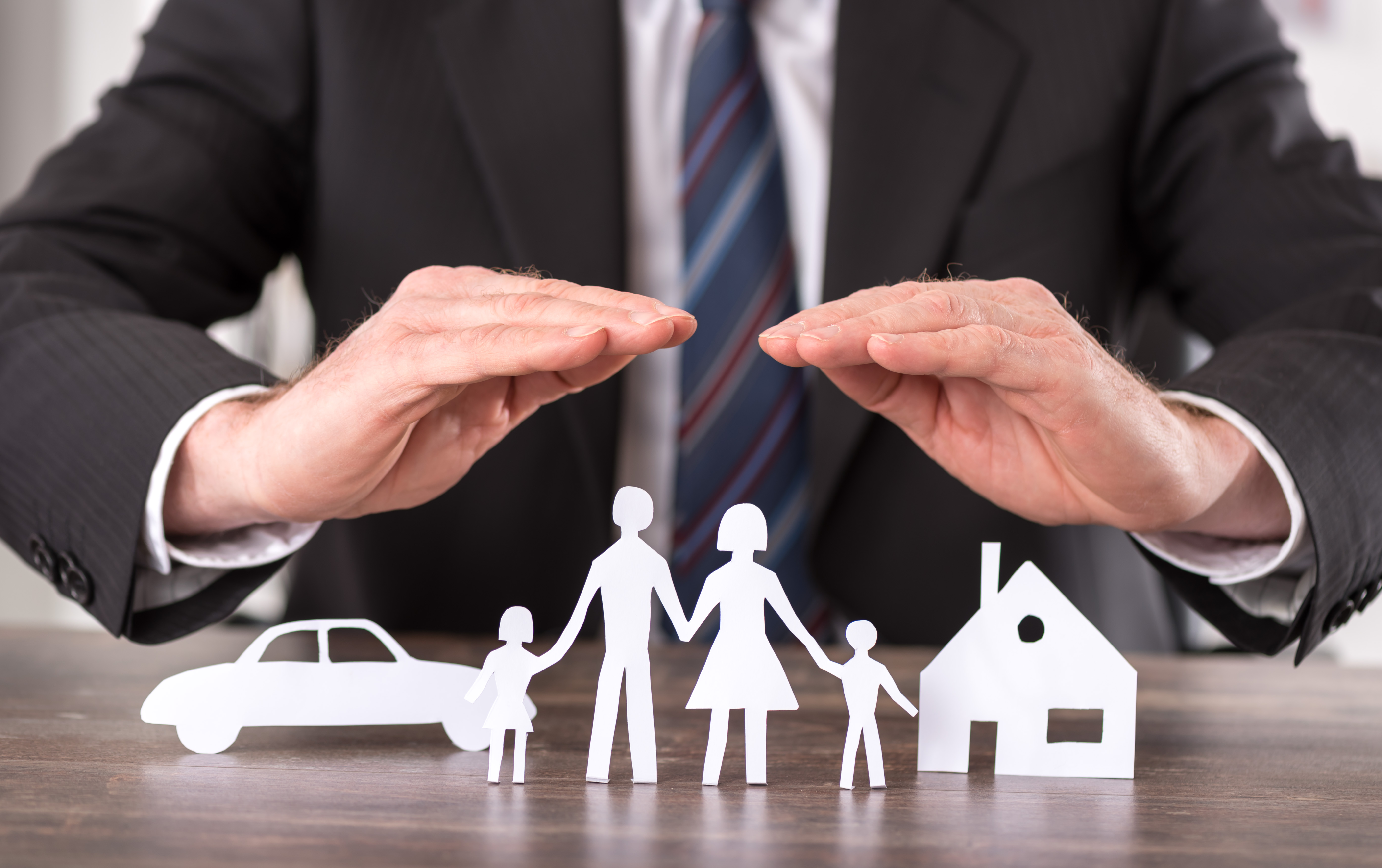 Concept of insurance with hands over a house, a car and a family