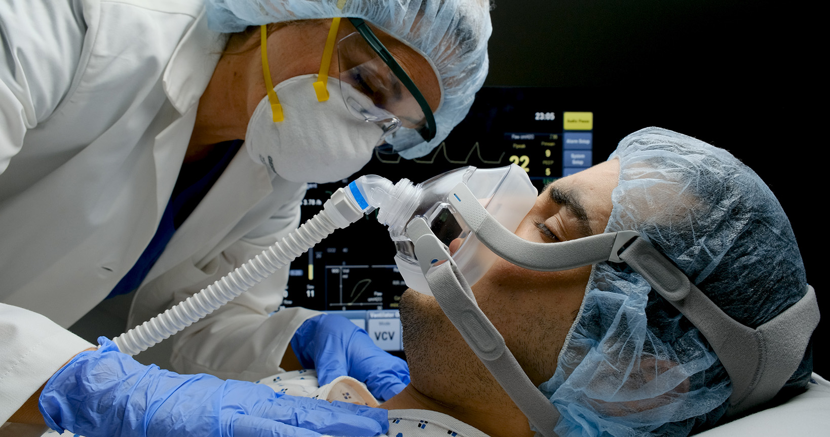 Female caucasian doctor checking on Covid-19 infected patient while connected to a ventilator at a hospital room