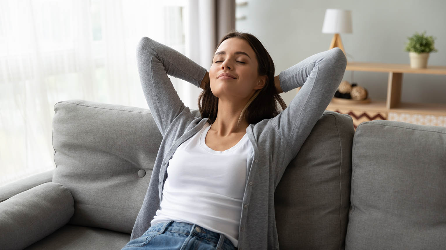 Relaxed serene pretty young woman feel fatigue lounge on comfortable sofa hands behind head rest at home, happy calm lady dream enjoy wellbeing breathing fresh air in cozy home modern living room