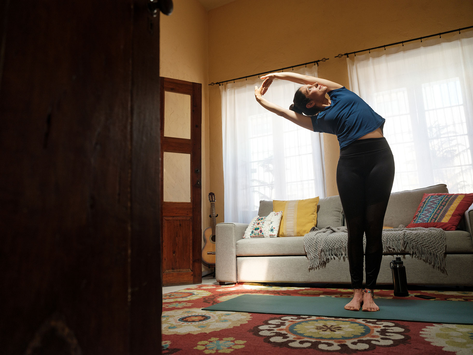 A fit young latin woman doing stretching exercises on a mat in the living room.