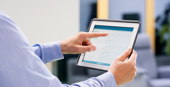 Close-up of man controlling home utilities with digital tablet.