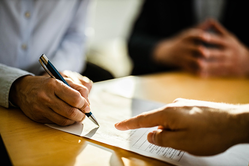 Close up of unrecognizable female person signing a contract on a meeting with agent.