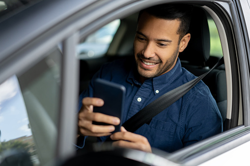 Portrait of a happy man texting and driving in his car on his cell phone â lifestyle concepts