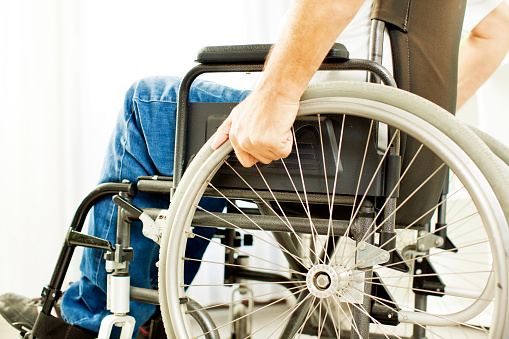 Man in a wheelchair. Unrecognizable person holding hand on a wheel. Side view and selective focus to arm.