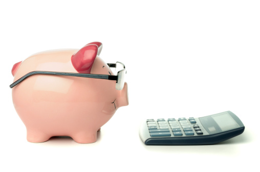 Piggy bank wearing glasses next to a calculator isolated on white.