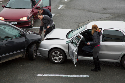 Two men looking at cars collision on road, woman standing near car.
