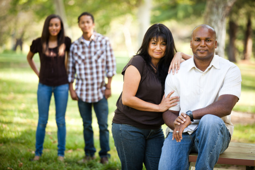 Guatemalan mother and African American father family photo in park. Focus on parents, children in background