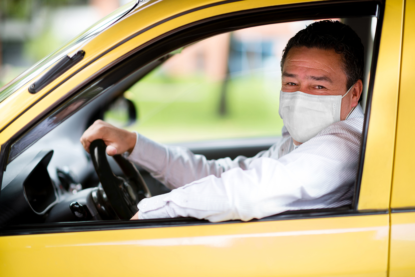 Happy taxi driver wearing a facemask in the car and looking at the camera through the window â COVID-19 lifestyle concepts