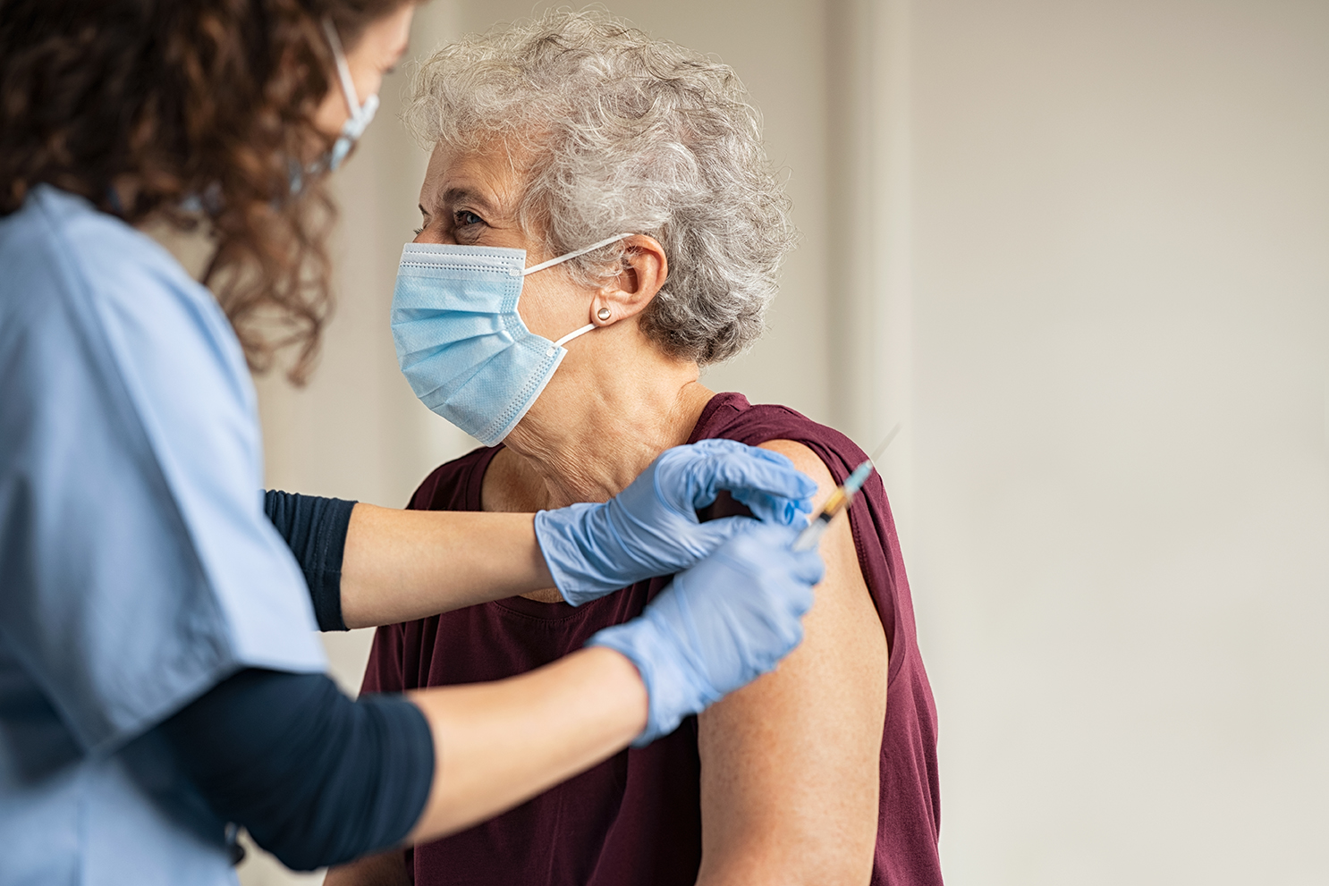 General practitioner vaccinating old patient in private clinic with copy space. Doctor giving injection to senior woman at hospital. Nurse holding syringe and using cotton before make Covid-19 or coronavirus vaccine.