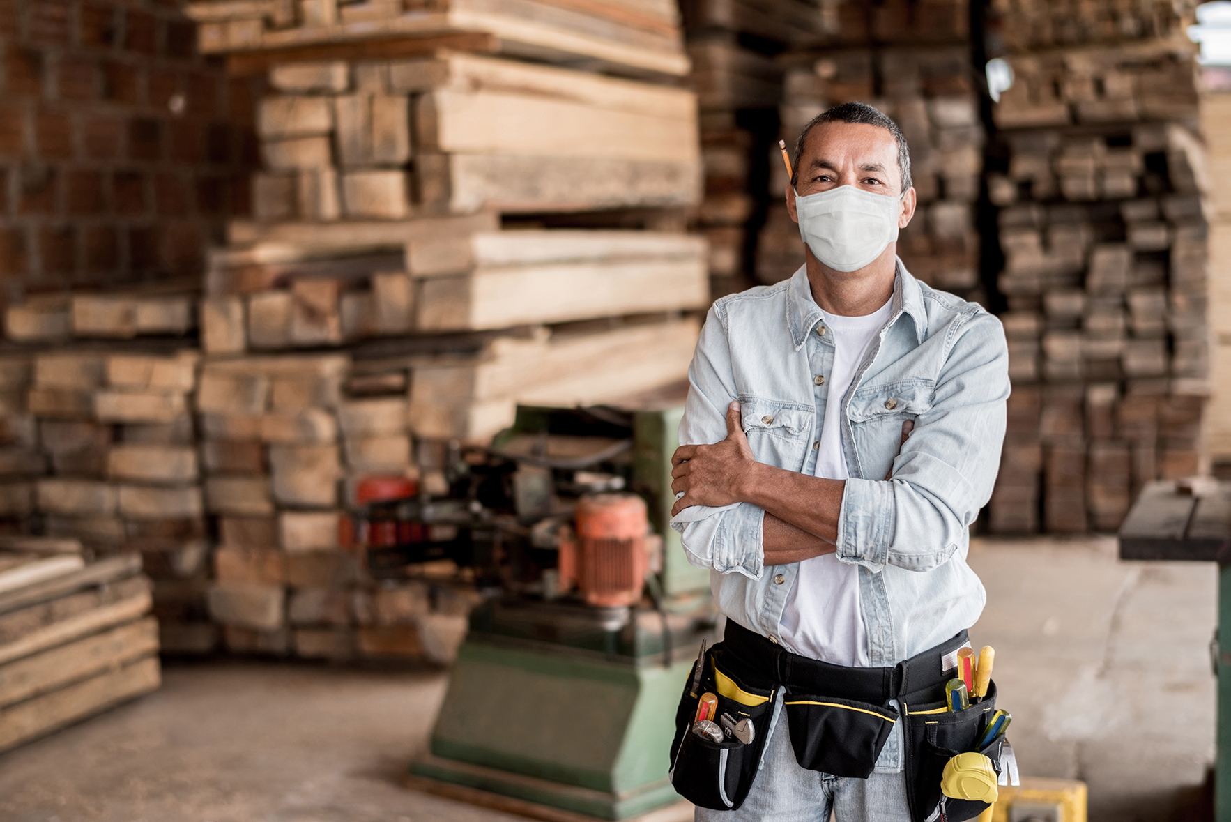 Happy Latin American carpenter working at his workshop wearing a facemask to avoid coronavirus - pandemic lifestyle concepts