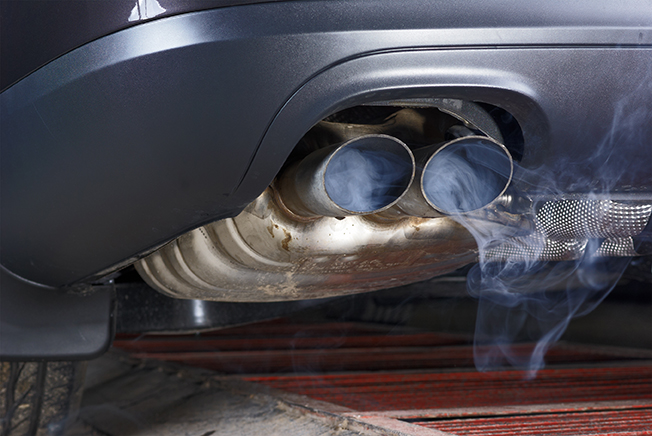 Exhaust pipe of a car - blowing out the pollution. Exhaust pipe coming out of the car with its exhaust. View from below, see the bottom of the exhaust pipe silver. Visible rear bumper eclipse of gray.