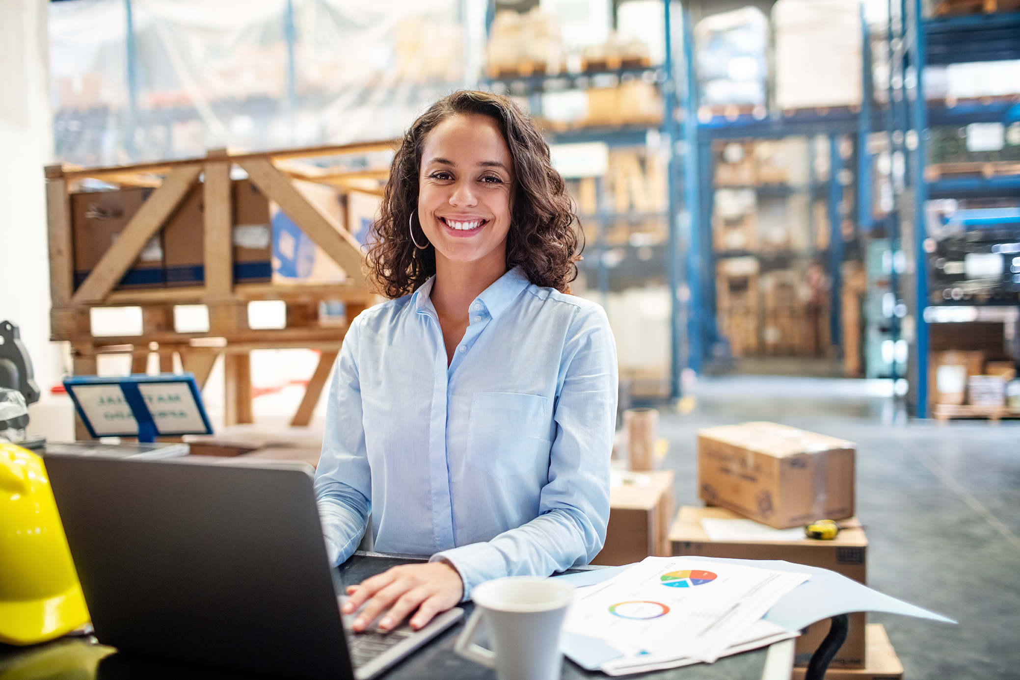 Smiling business woman working on laptop at a warehouse. Businesswoman with a laptop working at a distribution warehouse.