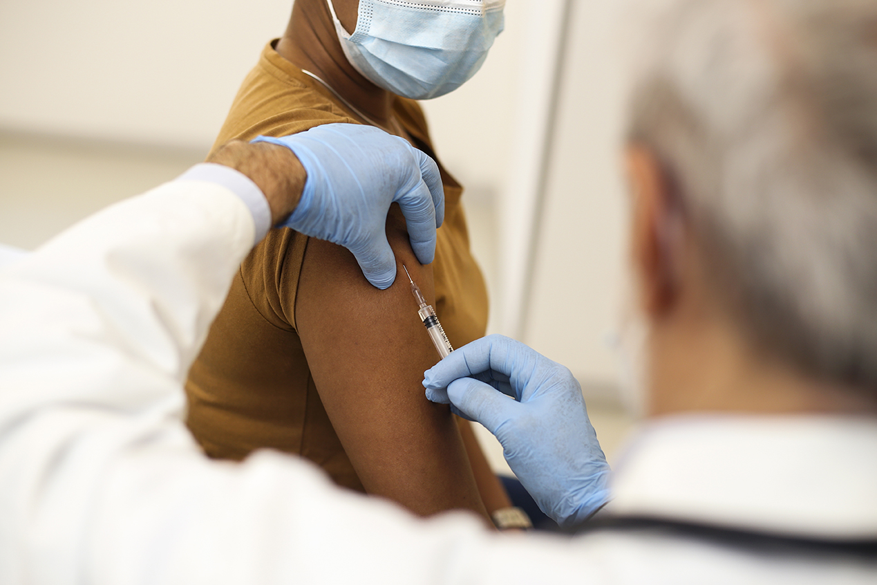 Mid adult woman on a COVID-19 vaccination in a doctor's office during the pandemic. About 35 years old African female patient and a 65 years old Caucasian male doctor.