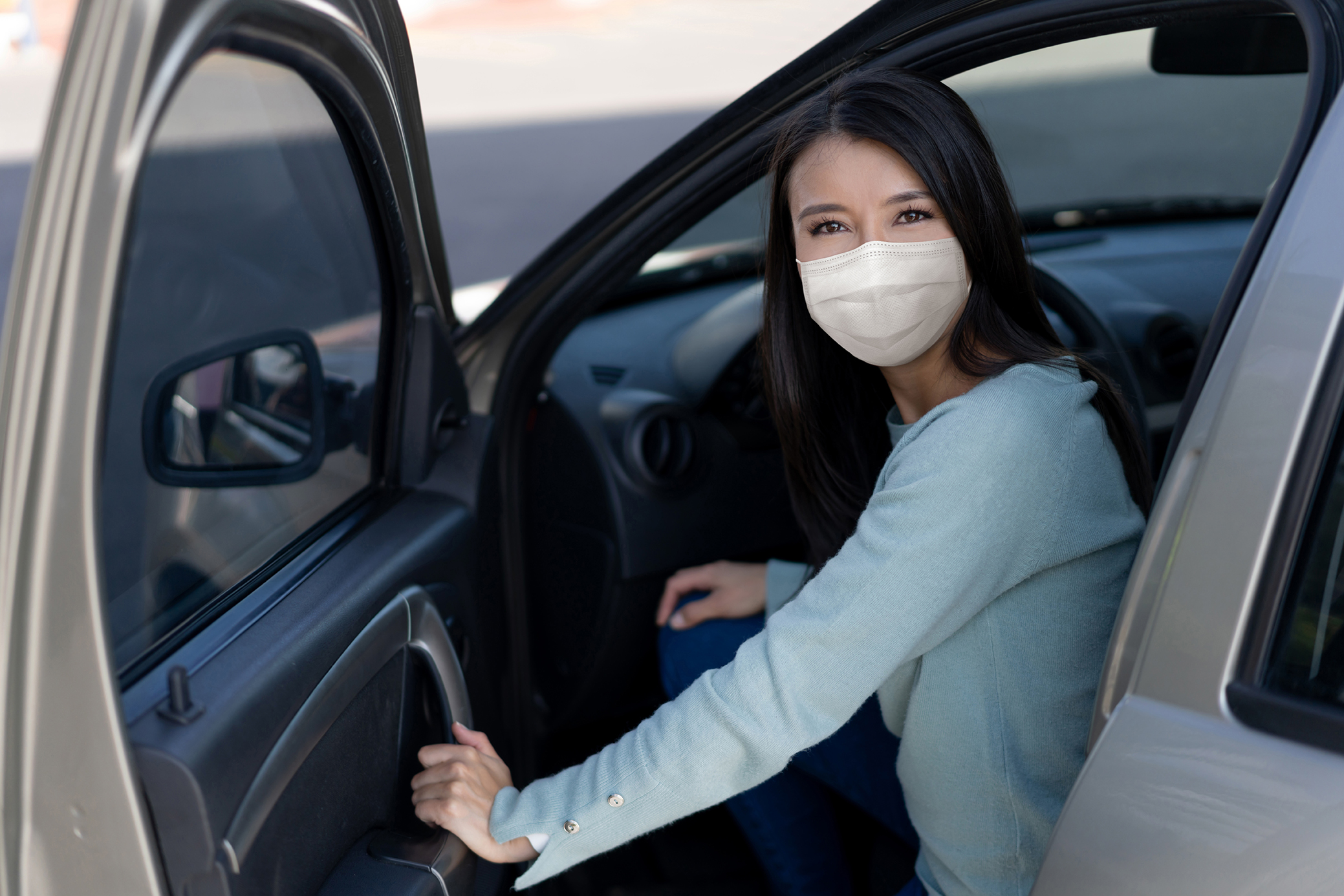 Portrait of a Latin American woman getting in her car wearing a facemask and looking at the camera - COVID-19 pandemic lifestyle