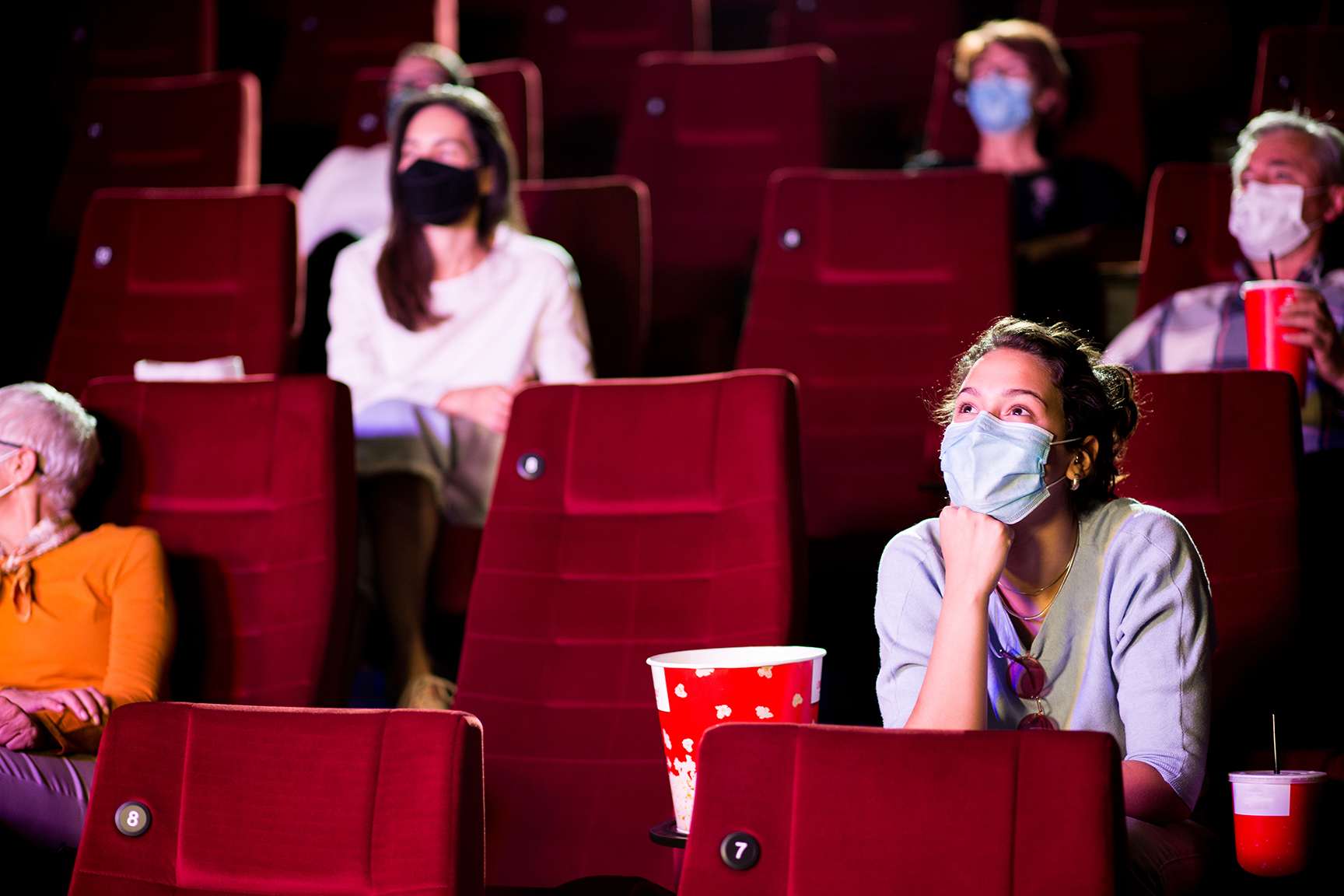 Audience at the cinema wearing protective face masks and sitting on a distance while watching the movie.