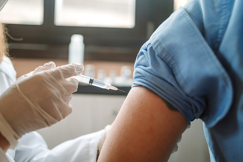 Mature man getting a COVID-19 vaccine by a female nursing doctor at home