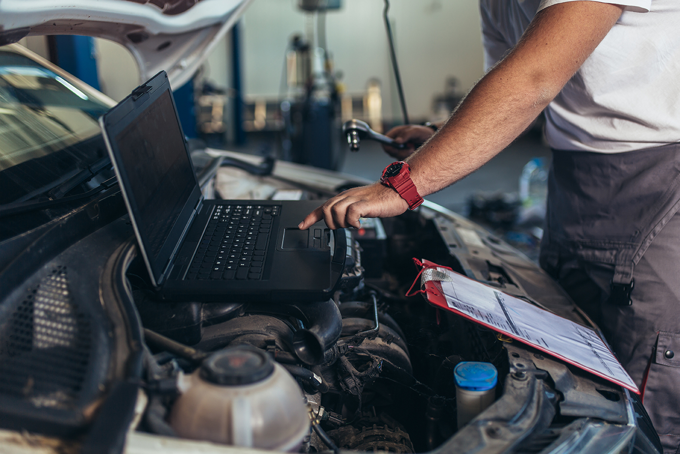 Professional car mechanic working in auto repair service using laptop.