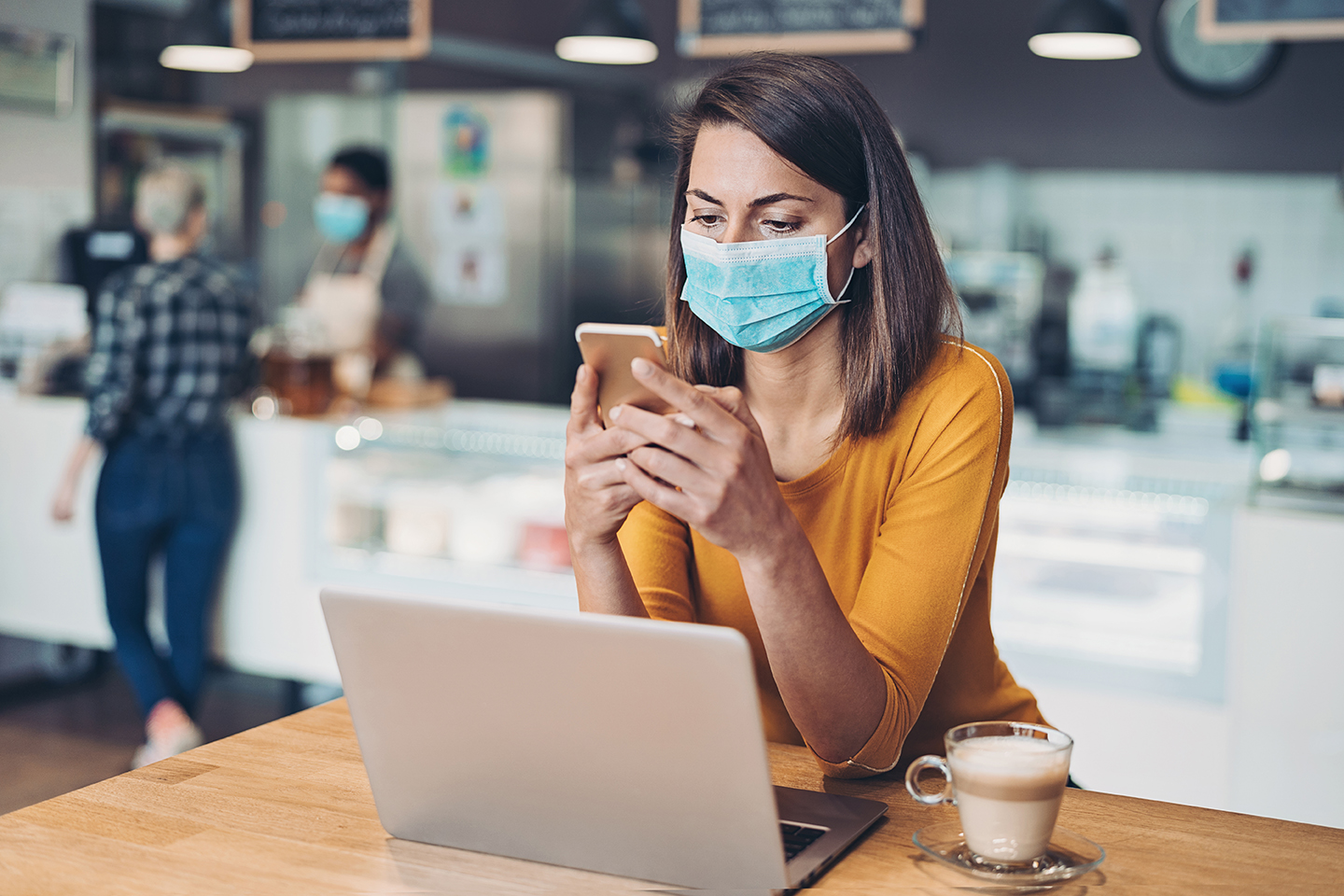 Woman wearing a face mask working on a laptop in cafe