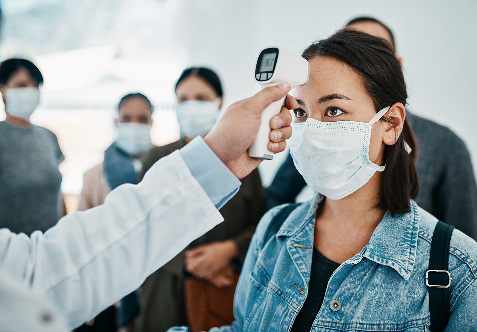 Shot of a young woman getting her temperature taken with an infrared thermometer by a doctor during an outbreak