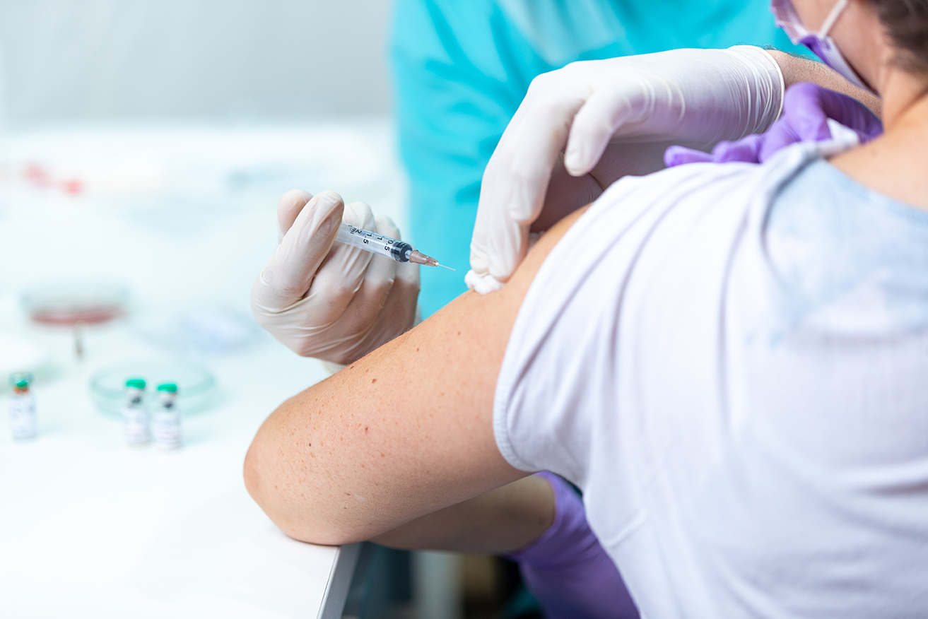 Hand in surgical glove holding cotton pad on arm after vaccination with syringe