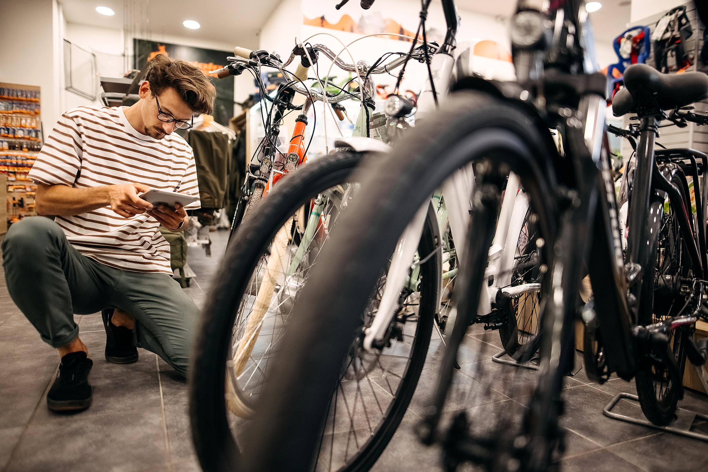 A man in a bicycle shop is looking at which bicycle to buy