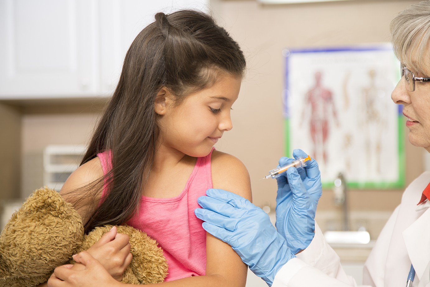 Female, senior adult doctor, latin descent little girl patient in pediatrician's office, medical clinic or hospital.  The doctor gives the child a vaccine.