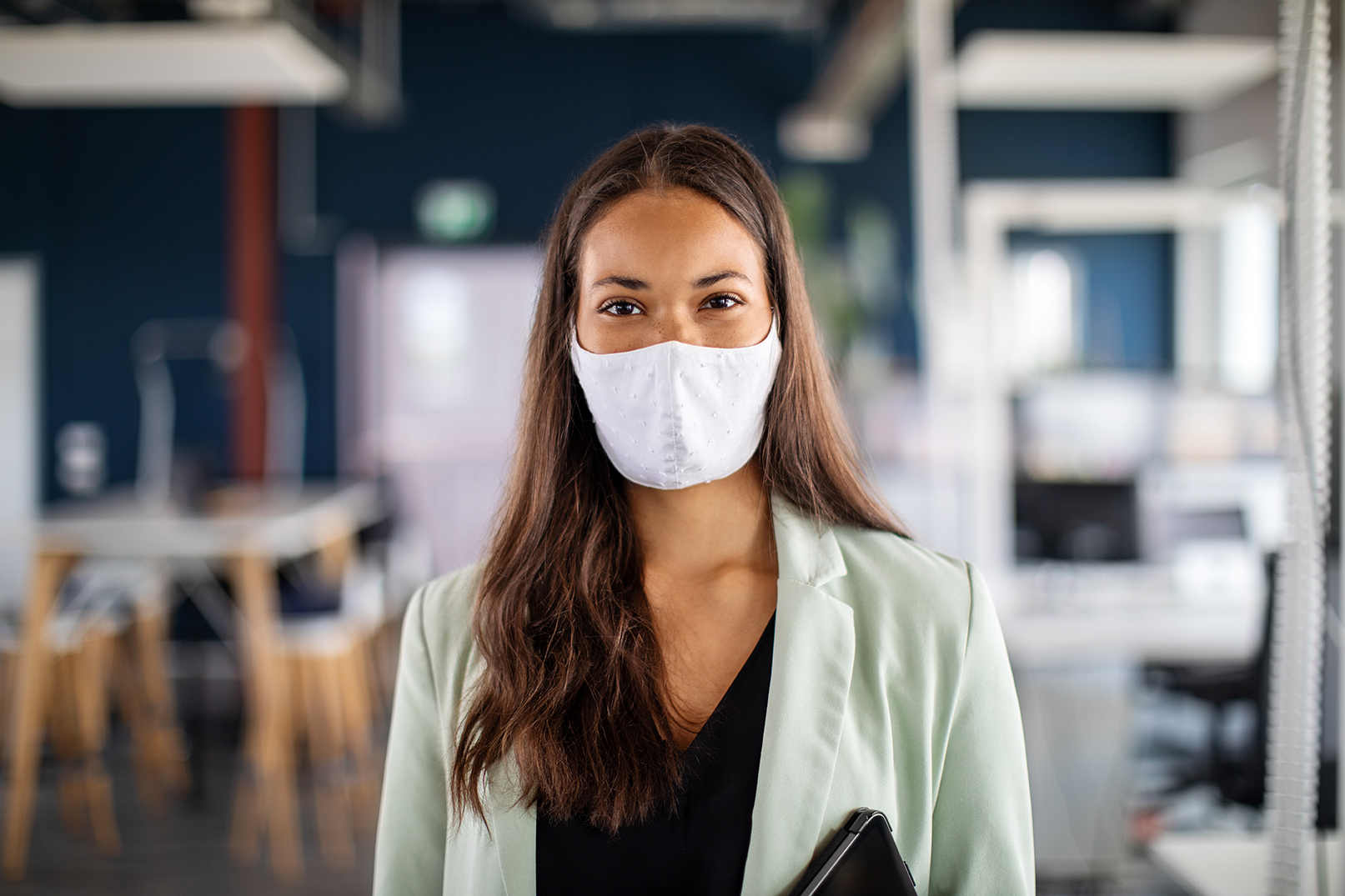 Close-up portrait of a businesswoman with face mask in office. Woman with protective face mask standing in office and looking at camera.