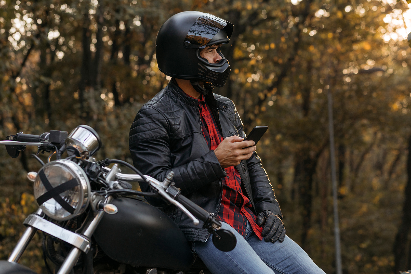 Caucasian male biker sitting on his motorbike and using his smart phone