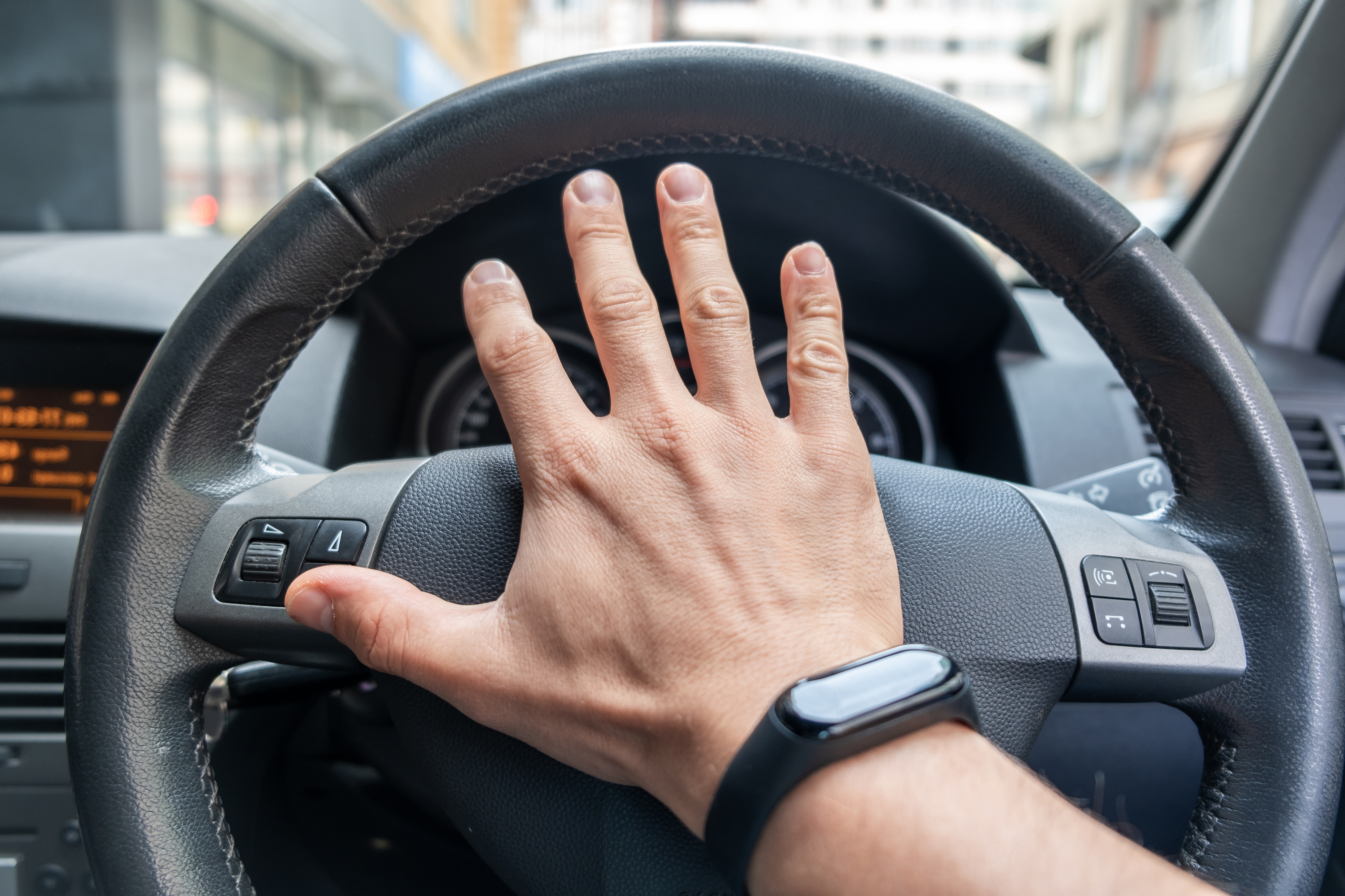 Drivers hand on a steering wheel of a car.