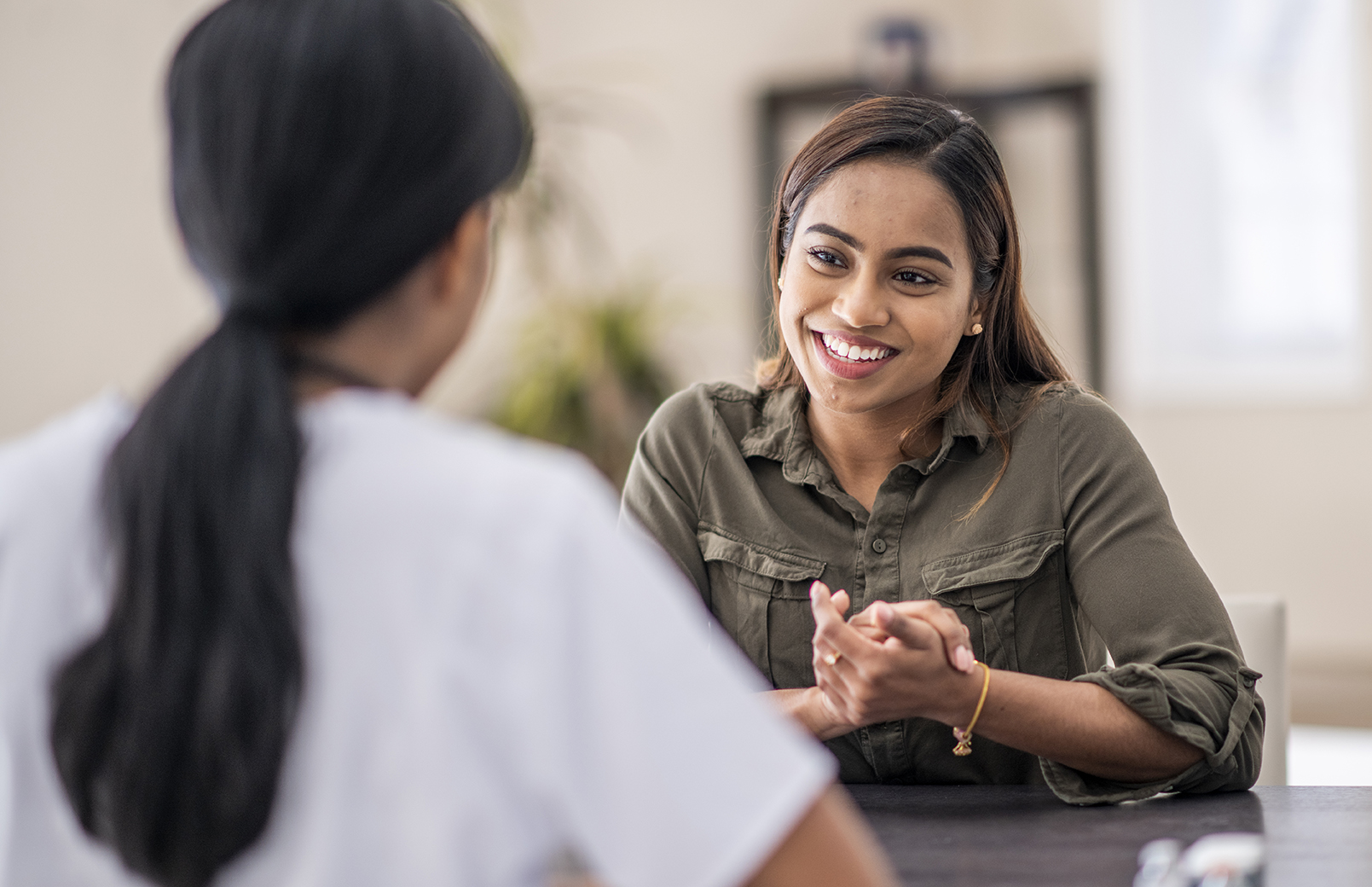 A stressed-out woman is chatting with her mental health counselor. She is explaining her problems. She is staying positive with a smile.