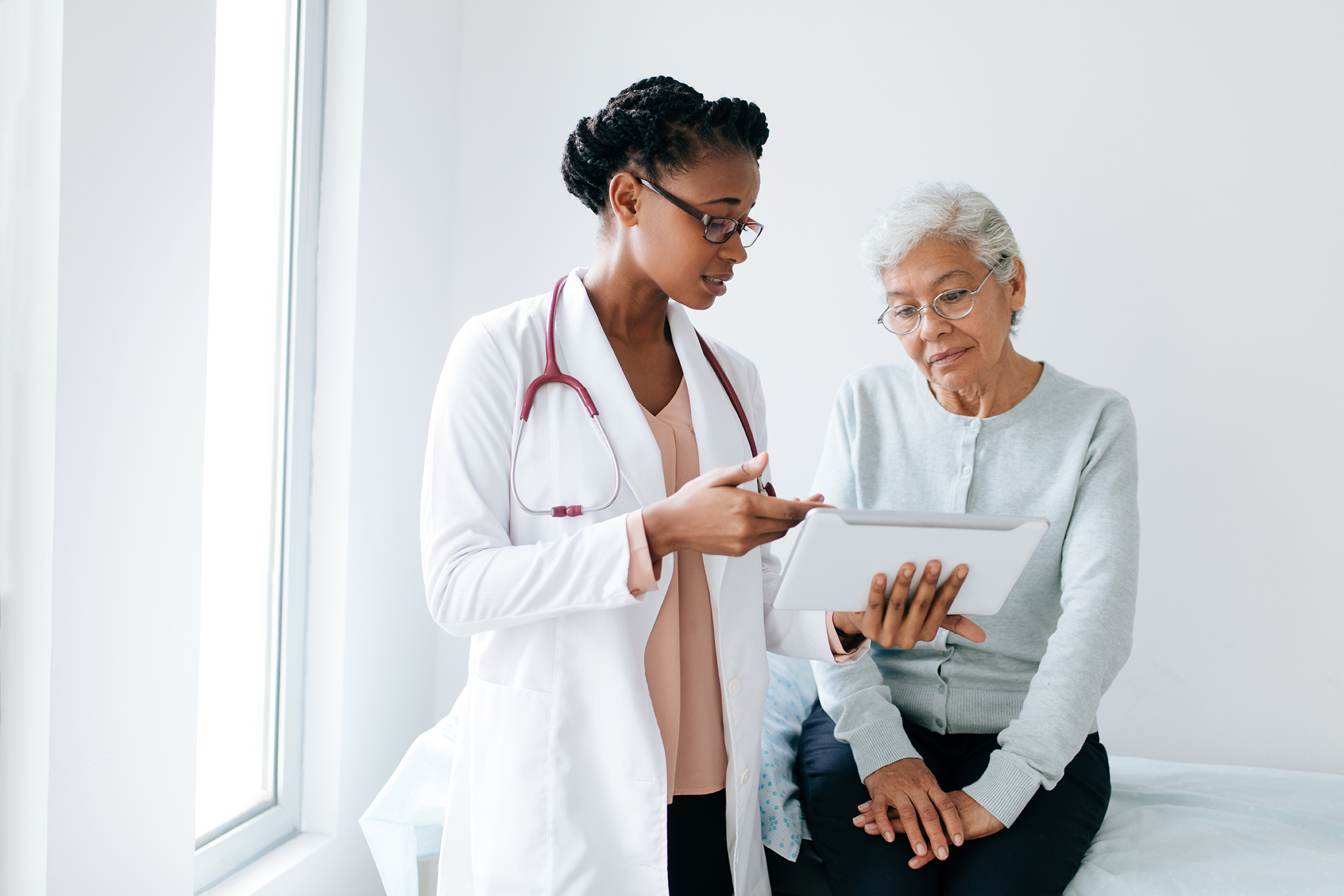 A black female doctor standing next to female patient and showing her something on digital tablet.