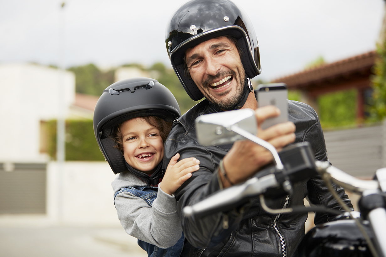 Happy father and son taking self portrait through mobile phone while riding motorbike