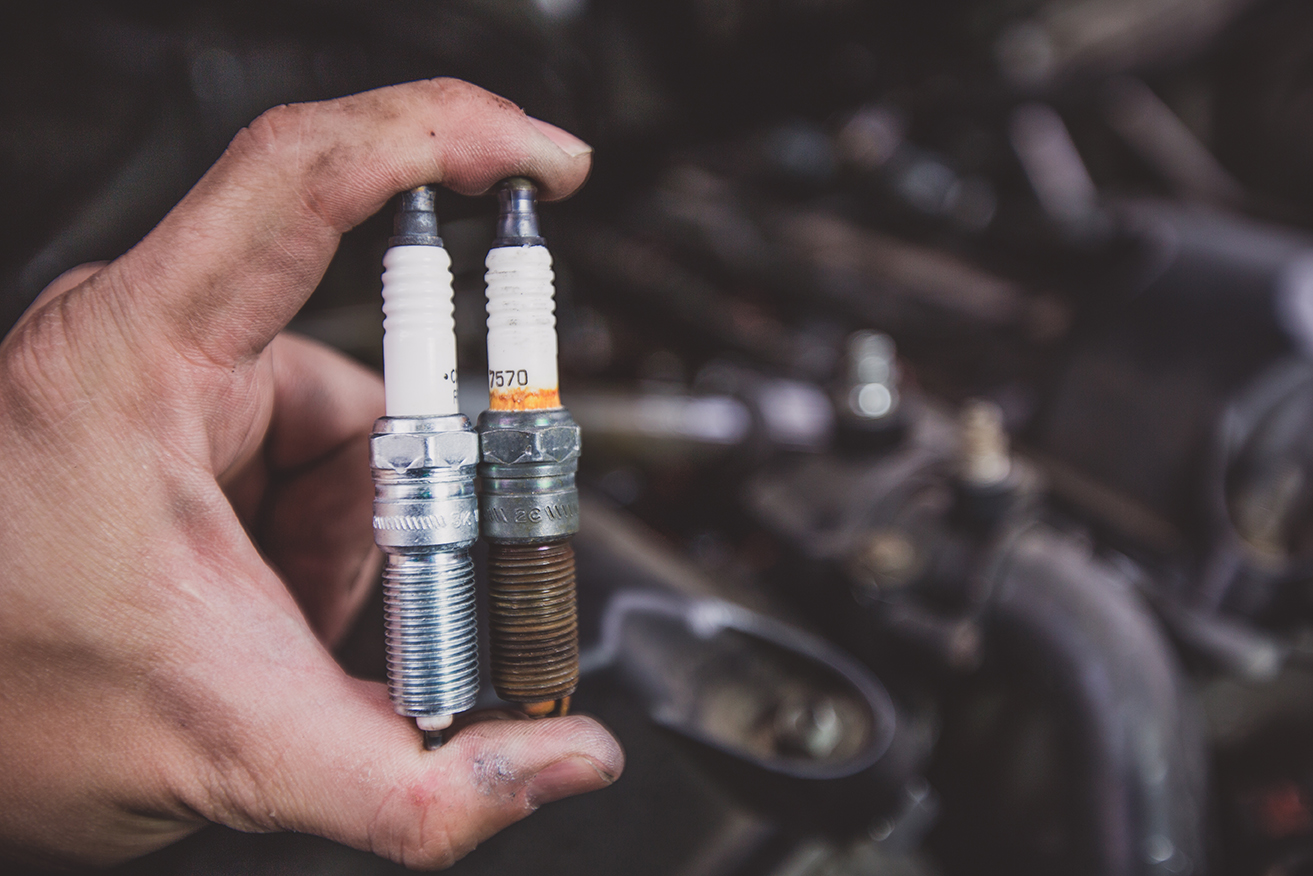 Holding old and new car spark plugs on engine