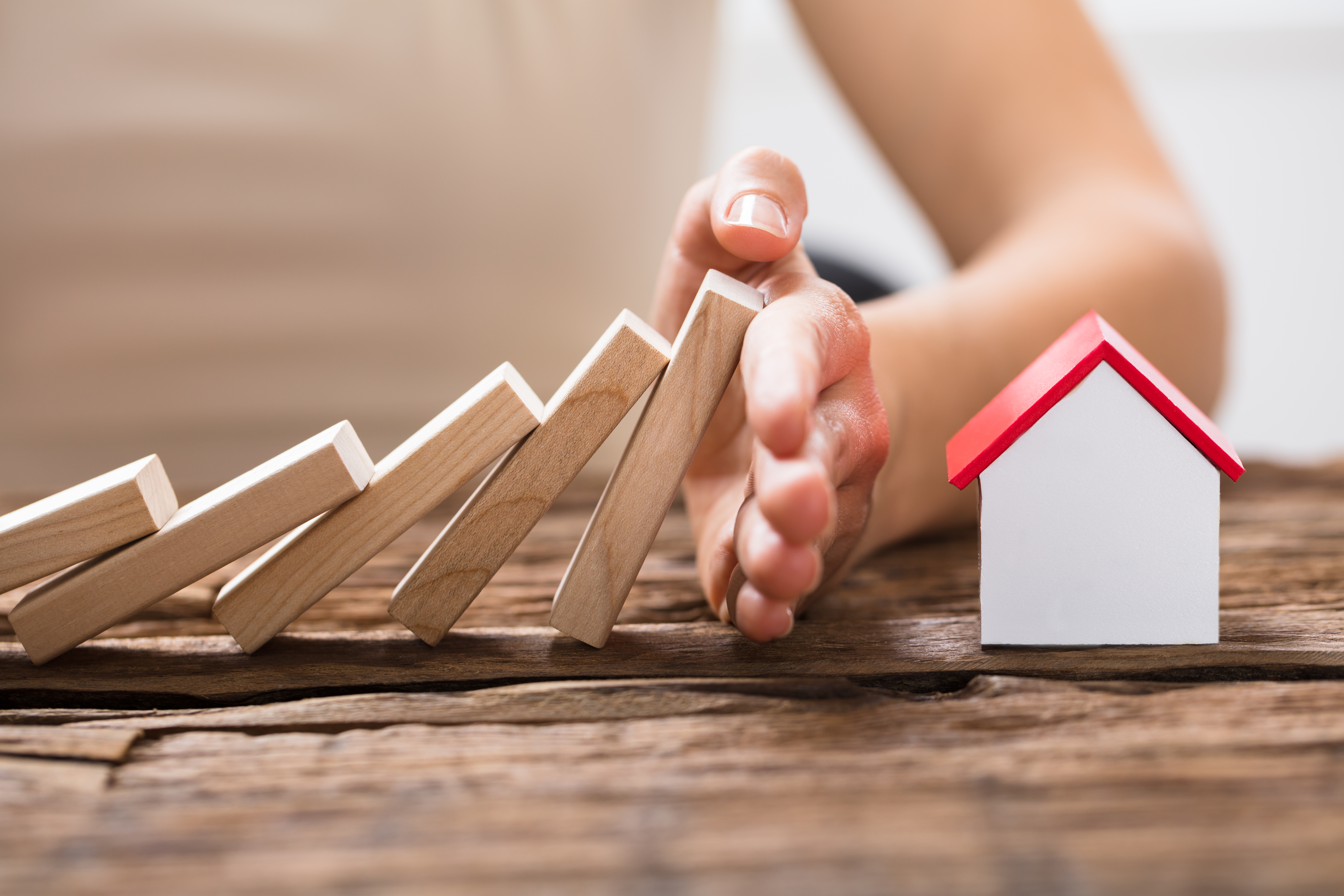 Close-up Of A Human Hand Stopping The Wooden Blocks From Falling On House Model